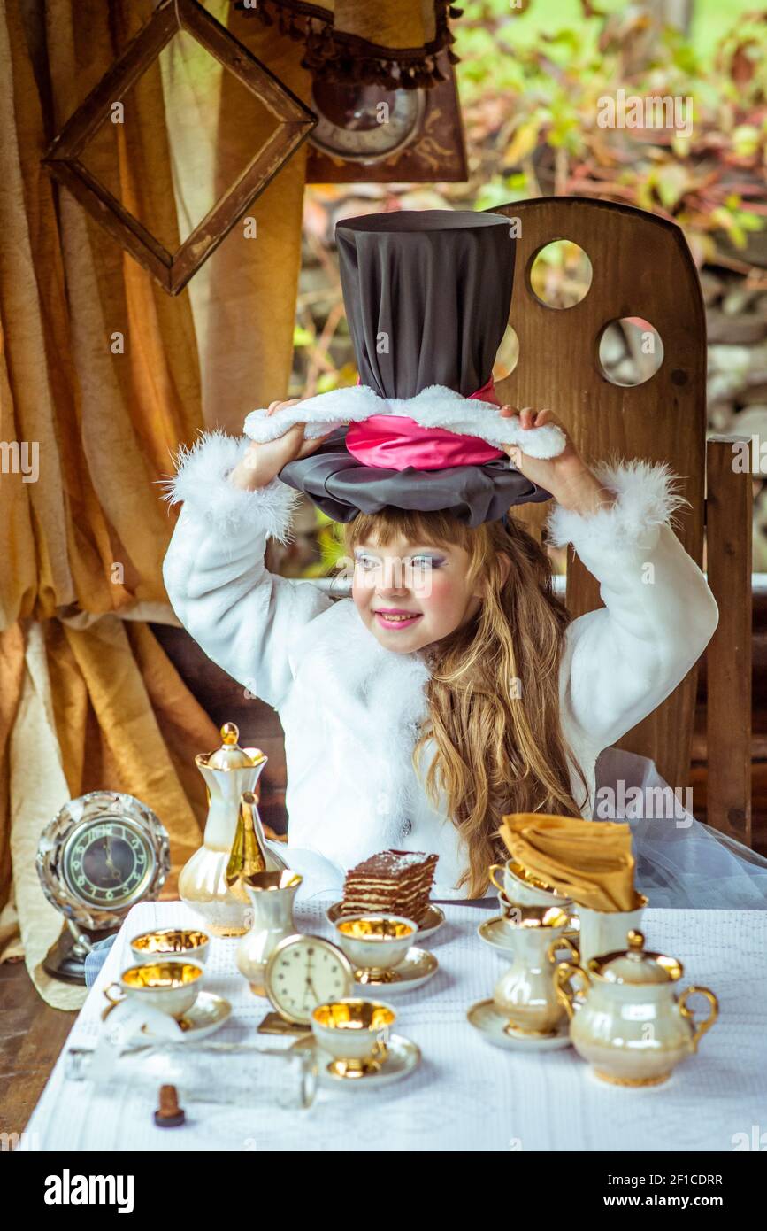 An little beautiful girl holding cylinder hat with ears like a rabbit over head at the table Stock Photo