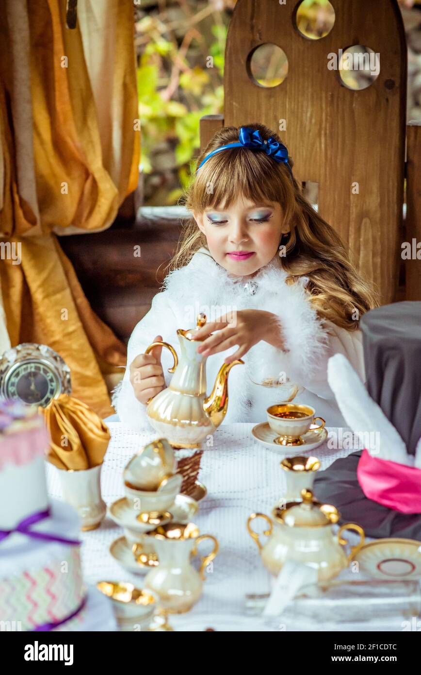 Front view of an little beautiful girl in the scenery of Alice in Wonderland pouring tea into a cup at the table Stock Photo