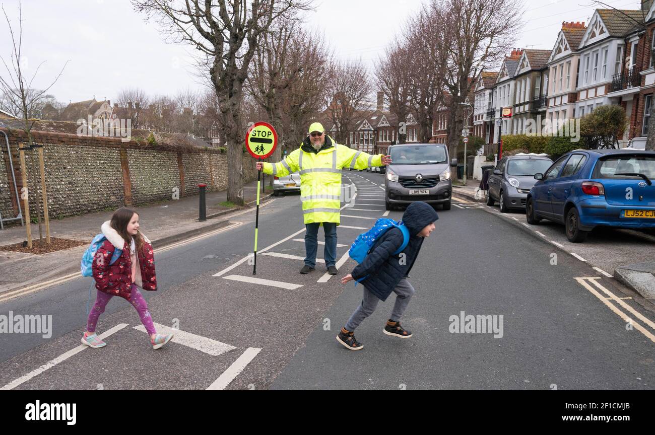 Brighton UK 8th March 2021 - Lollipop man Simon Moss welcomes back children to St Luke's Primary School in Brighton this morning as the government lockdown restrictions in England are starting to be eased . Schools and colleges are being reopened to all students today throughout England : Credit Simon Dack / Alamy Live News Stock Photo