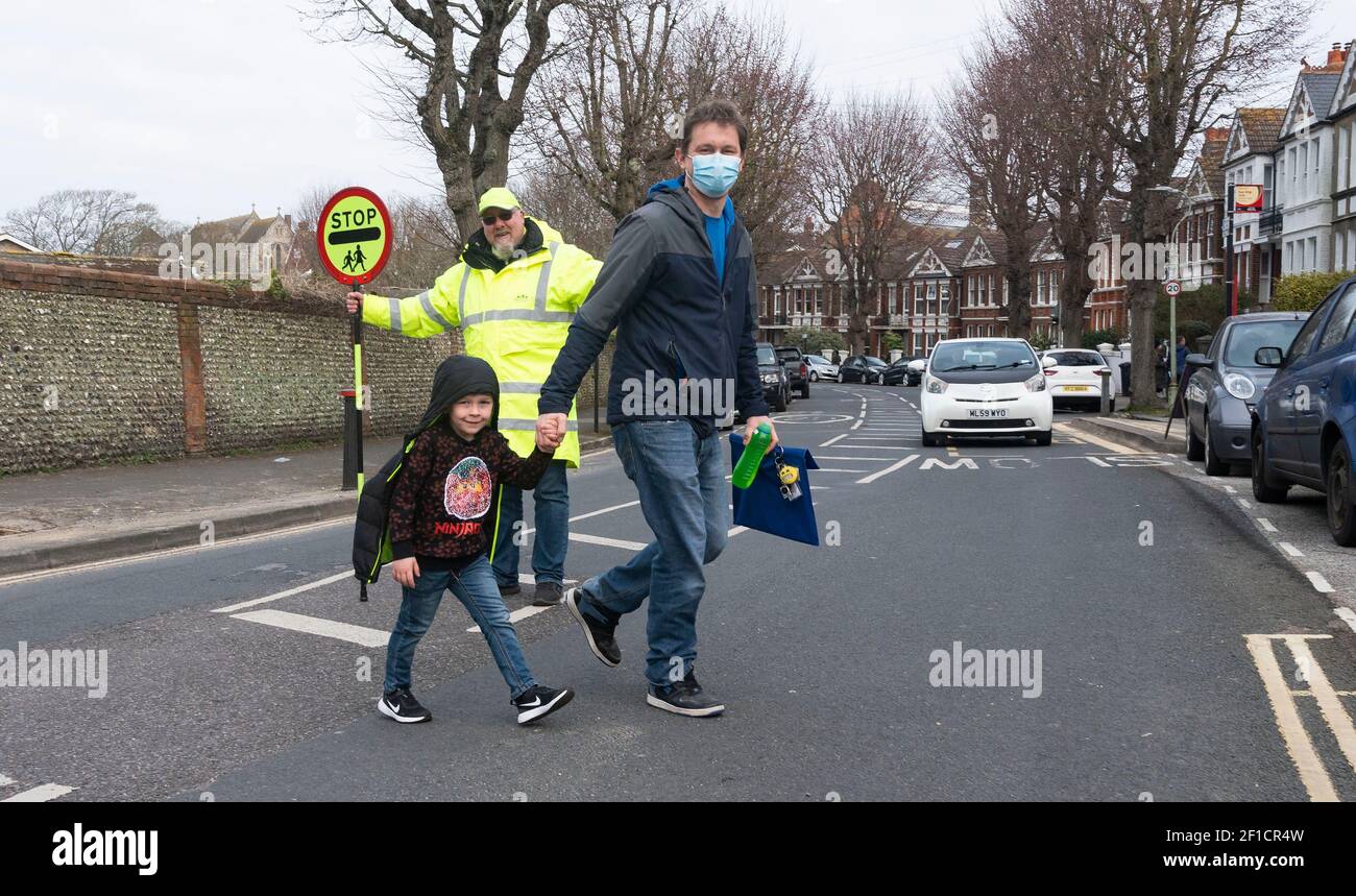 Brighton UK 8th March 2021 - Lollipop man Simon Moss welcomes back children to St Luke's Primary School in Brighton this morning as the government lockdown restrictions in England are starting to be eased . Schools and colleges are being reopened to all students today throughout England : Credit Simon Dack / Alamy Live News Stock Photo