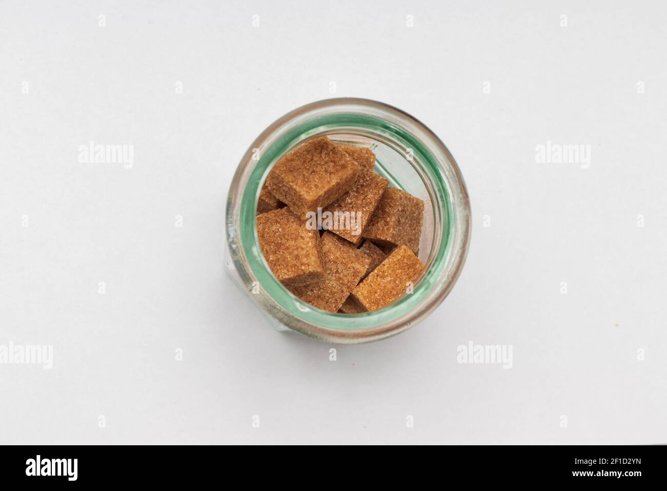 Glass cup with brown sugar cubes and cork top lid against white background topview Stock Photo