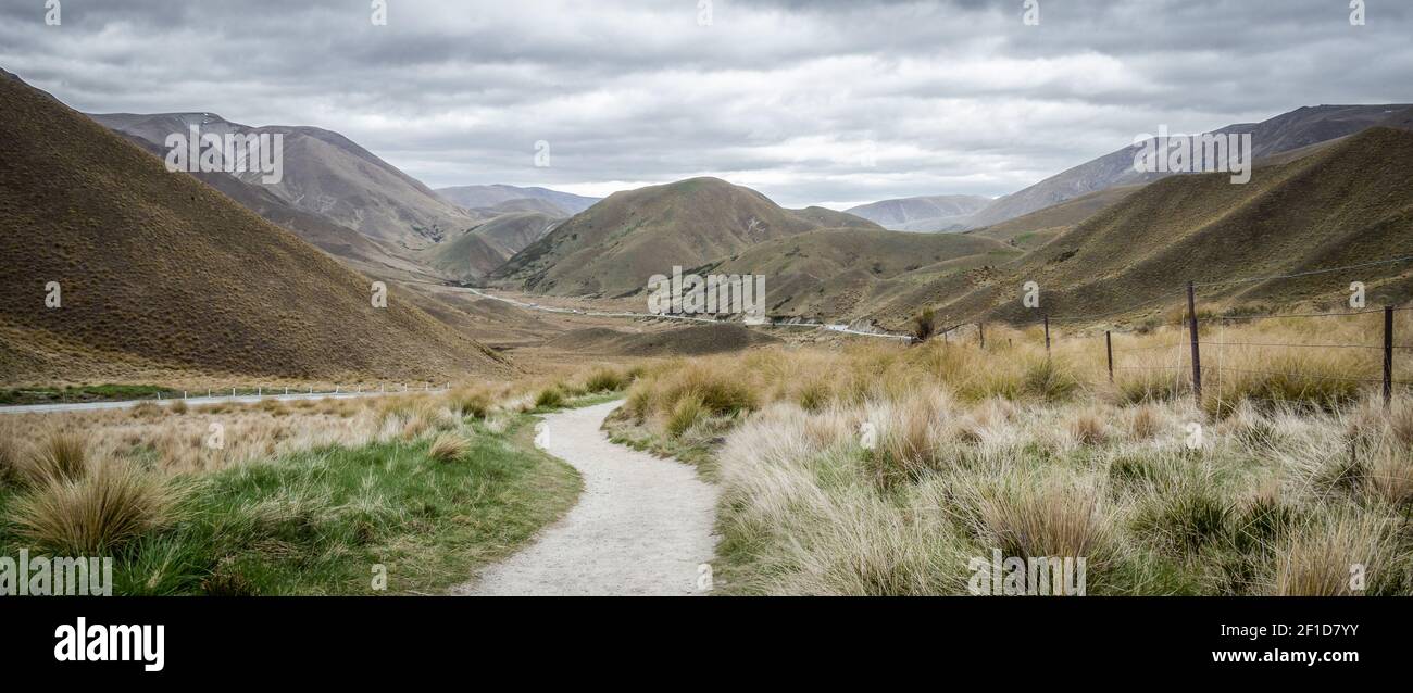 Panorama of dry valley with path leading to the centre of frame. Shot on overcast day in Lindis Pass, New Zealand Stock Photo