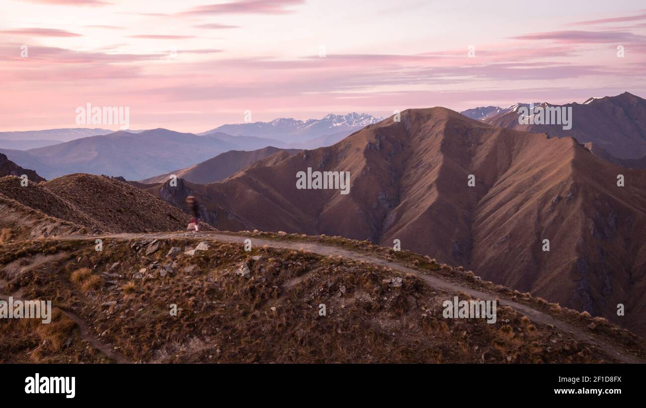 Person walking on the mountain trail during sunrise. Shot made during on Roys Peak summit in Wanaka, New Zealand Stock Photo