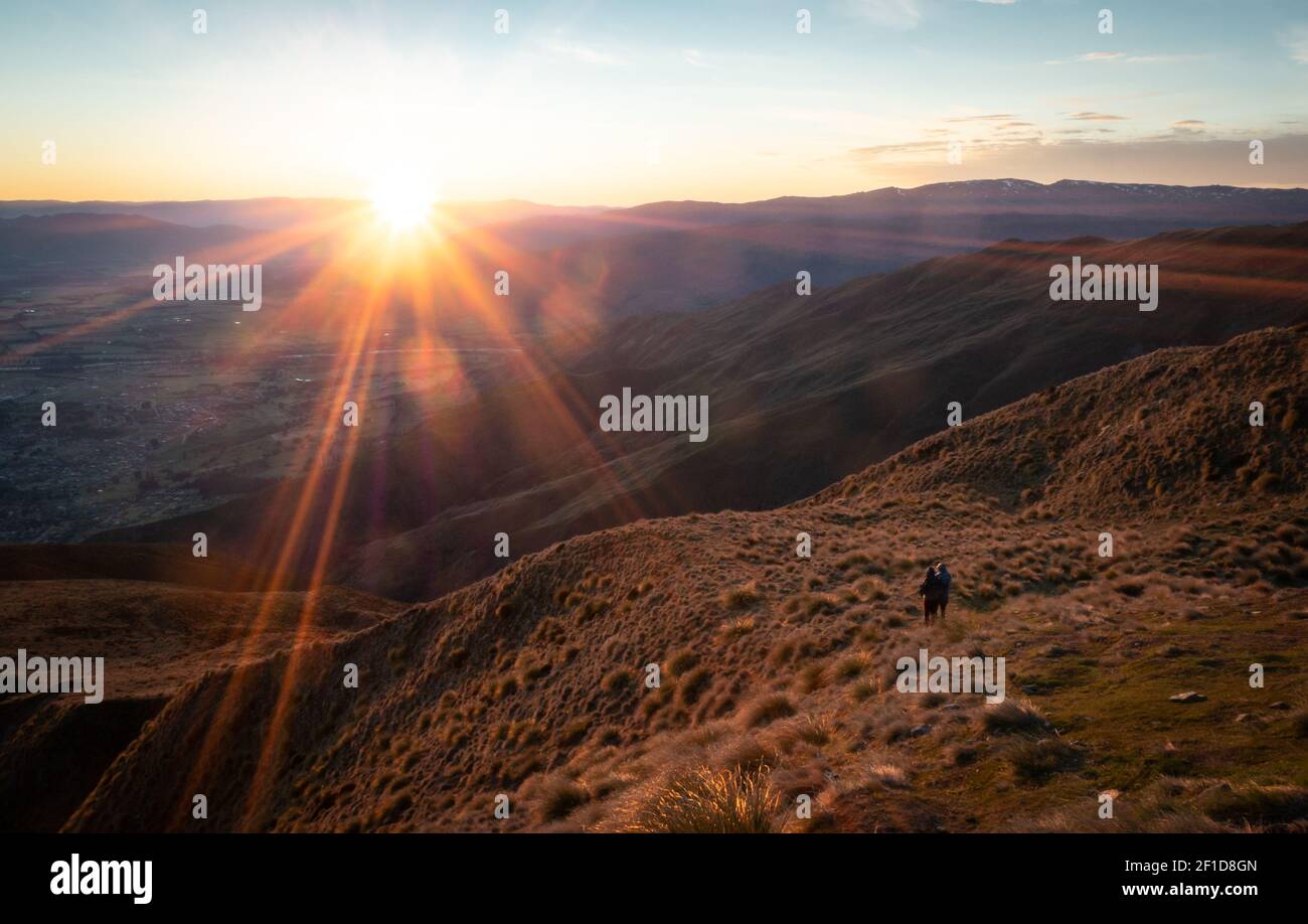 Couple watching sunrise on mountain summit, shot made on Roys Peak summit in Wanaka, New Zealand Stock Photo