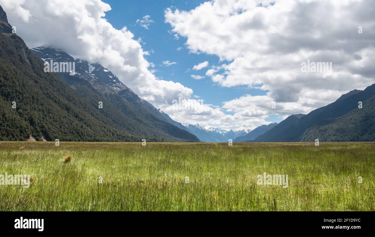 Beautiful picturesque valley surrounded by mountains with green fields in foreground and blue sky with some clouds. Photo taken in Eglinton Valley Stock Photo