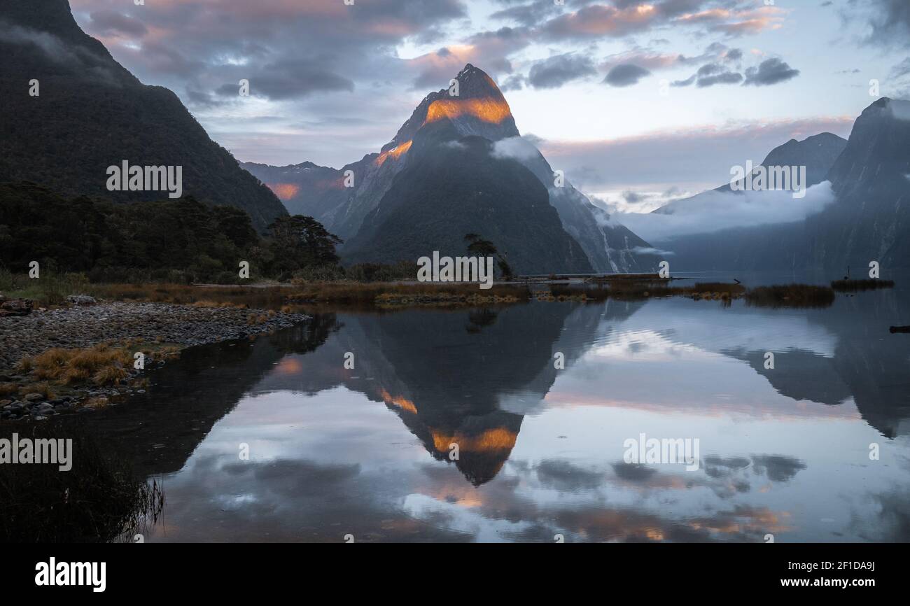First sunrays lighting the peak of mountain with beautiful reflection in water surface in front of it. Sunrise photo of Mitre Peak in Milford Sound Stock Photo