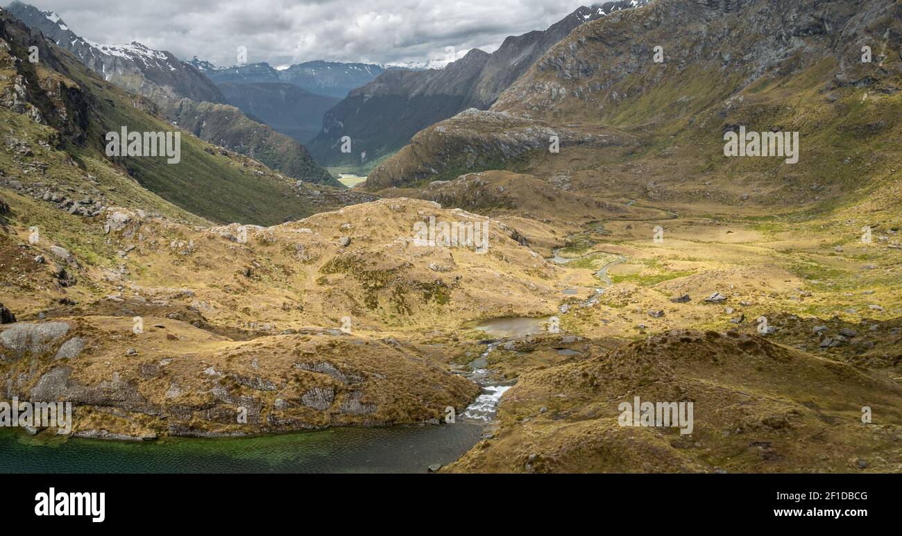 Beautiful alpine valley with layers of mountains and river flowing through it while illuminated partially by sun.  Shot on Routeburn Track,New Zealand Stock Photo