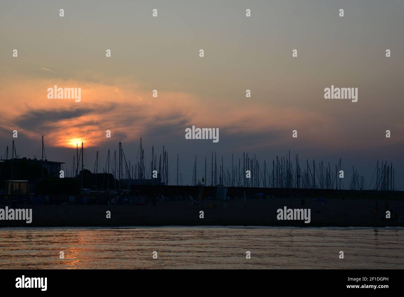 Romantic sunset over the harbor. Red-golden sunset in the background with masts of yachts and sailboats. Sunset on the Italian beach. Dark sea masts i Stock Photo