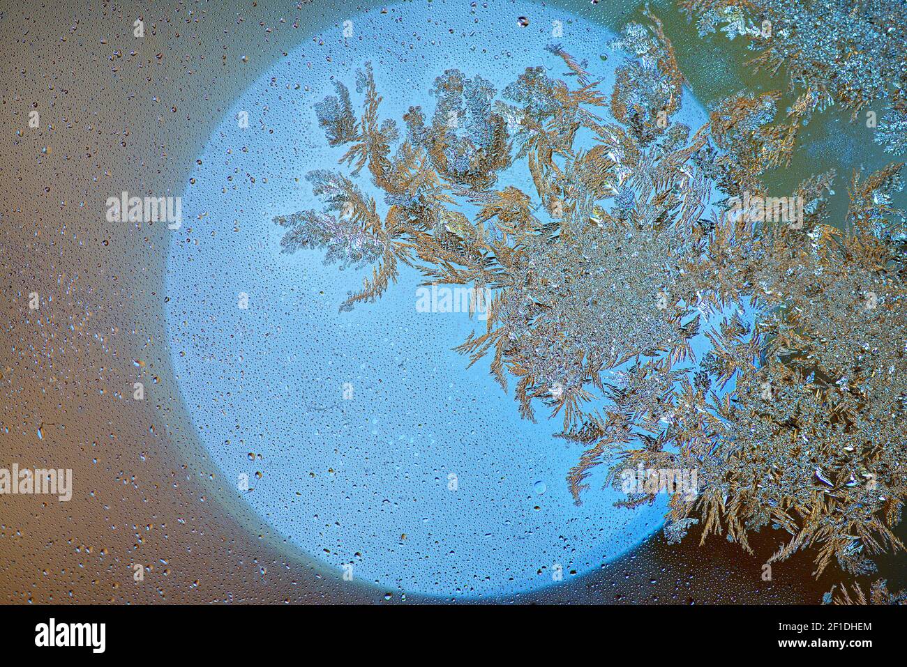 Ice crystals forming on a glass plate. Ice flowers on a yellow circle of light. Frost on the glass. Abstract background with shining sun, tiny water d Stock Photo