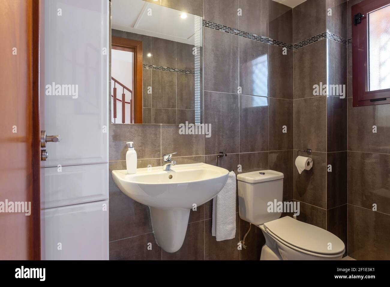 Beige colored bathroom interior, a shower with a glass door and a ceramic toilet, also a few towels on the walls. Stock Photo