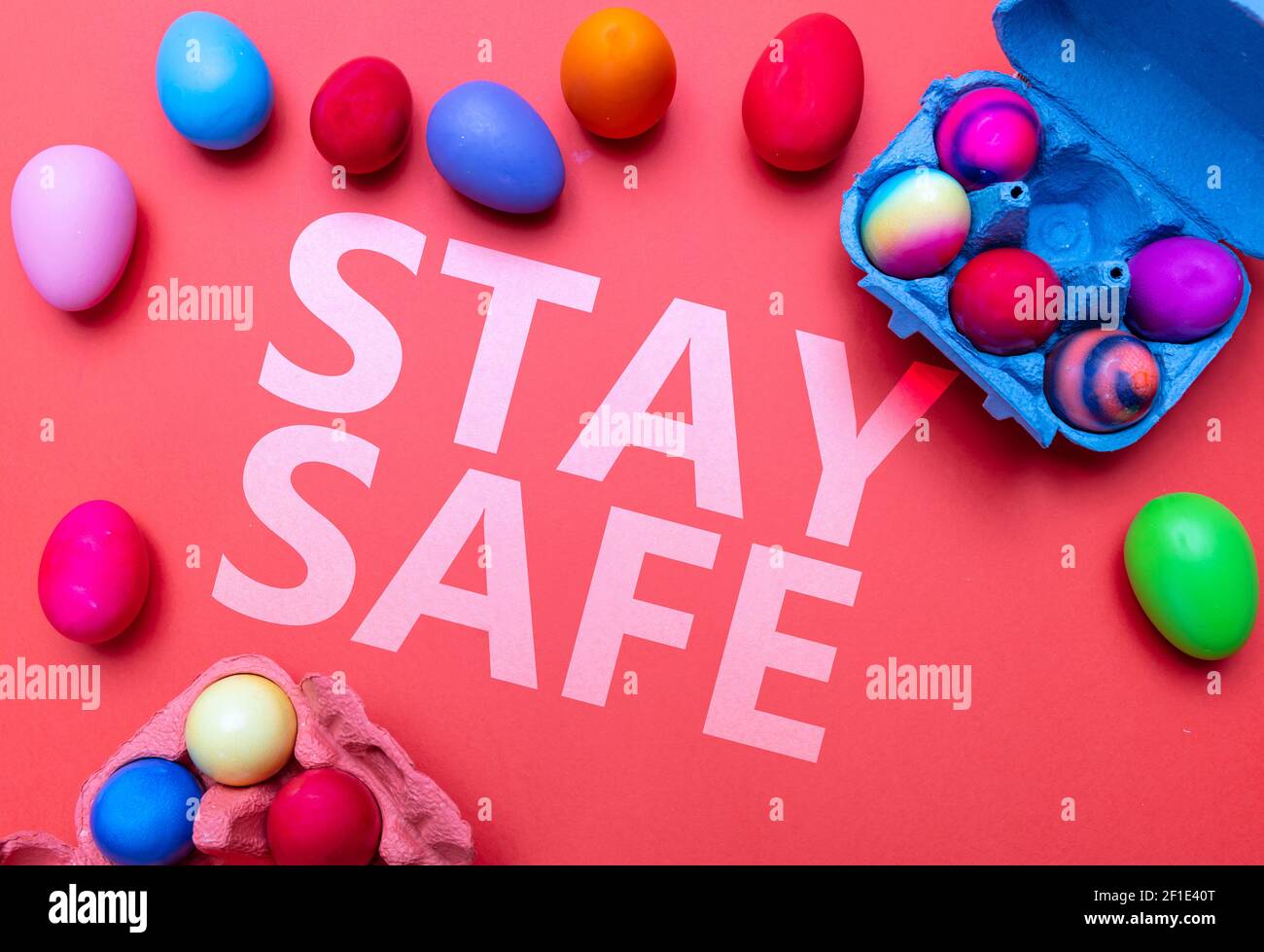 Easter at coronavirus days. Stay safe text message and Easter eggs on red orange color background, top view. Covid19 pandemic holiday celebration Stock Photo