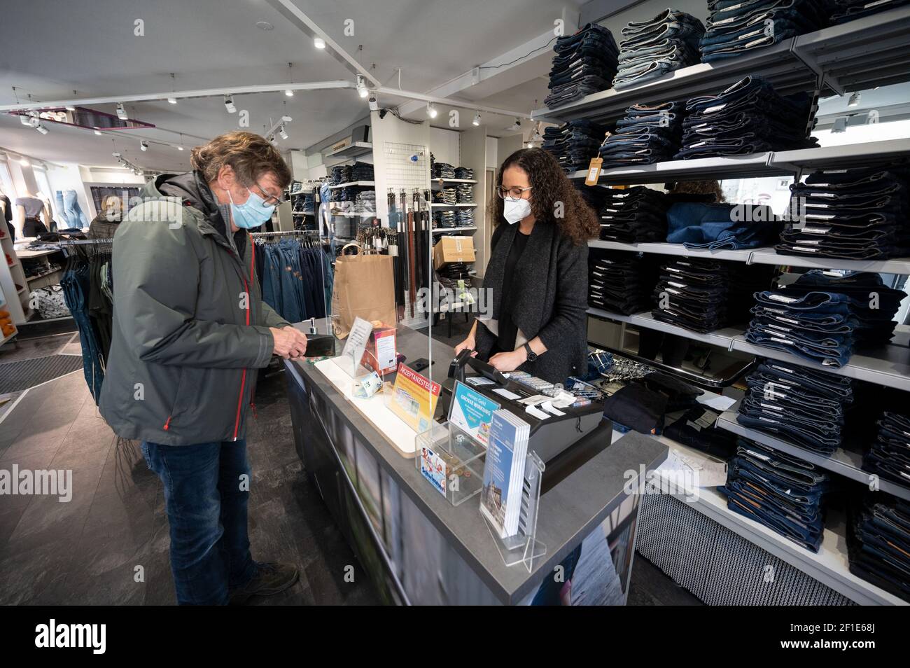 08 March 2021, Baden-Wuerttemberg, Tübingen: A customer pays for his goods to a saleswoman at the cash register in a downtown clothing store. Corona restrictions in Baden-Wuerttemberg are partially relaxed on Monday. Counties that have already been below an incidence of 50 for five or more days can open retail. Photo: Marijan Murat/dpa Stock Photo