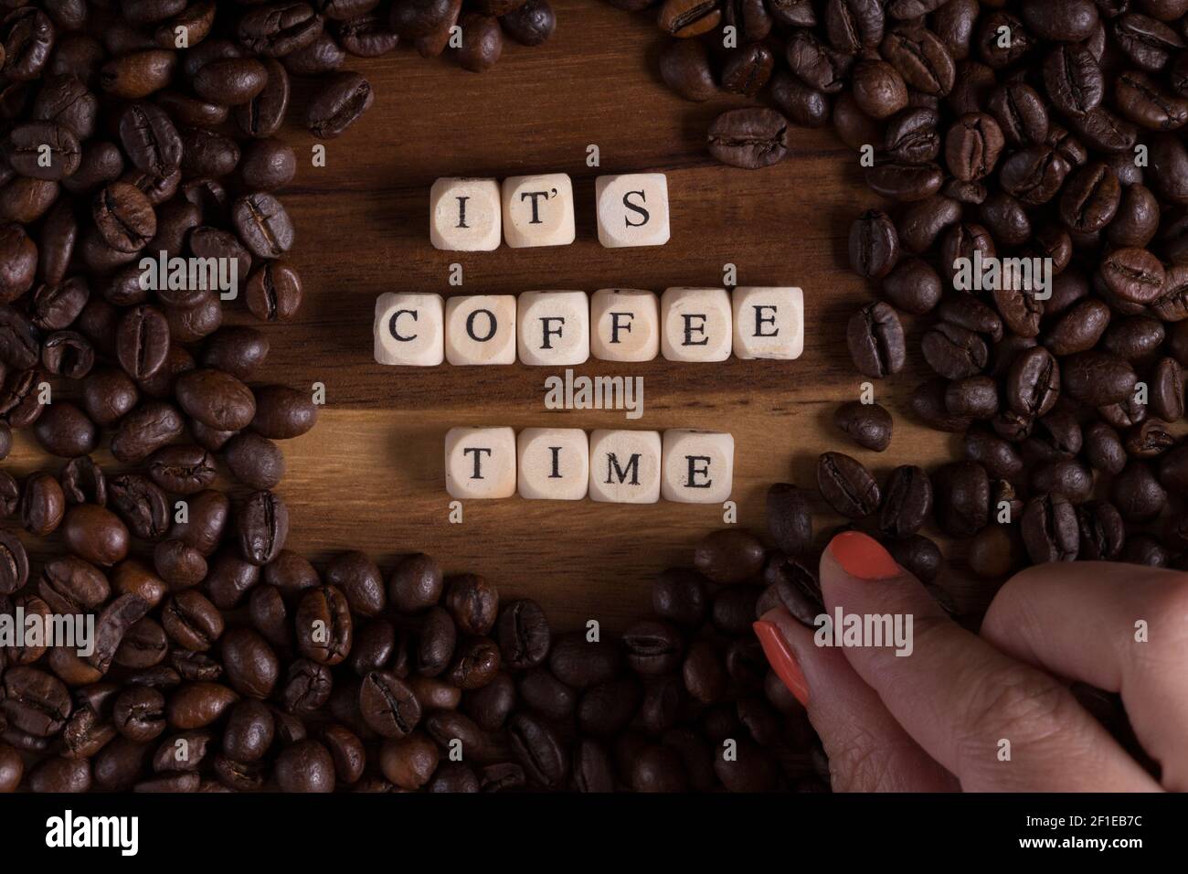 it's coffee time with a wooden cube letters and and a woman's hand with a coffee bean and coffee all around on a wooden table. good morning. Stock Photo