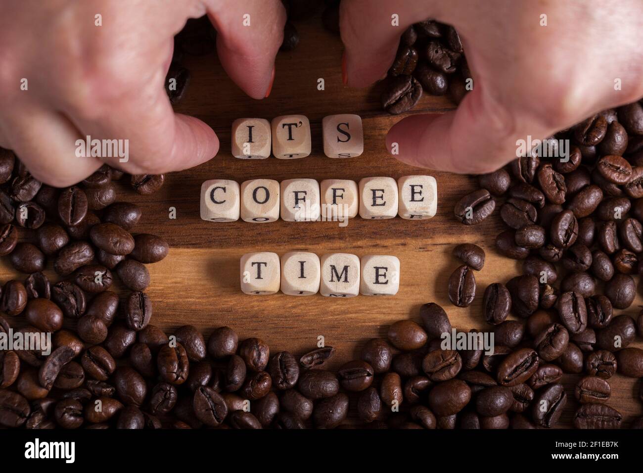 Female hands placing some wooden cubes with the phrase it's coffee time and Beans Coffee all around on a wooden table. Text Stock Photo