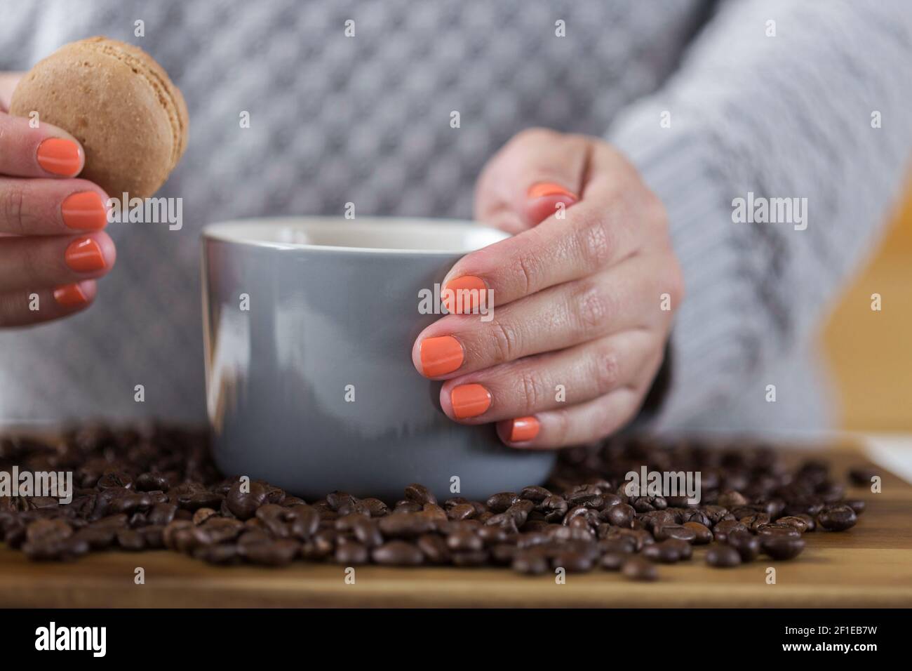 Female hand holding a mug of coffee and a macaroon. coffee beans on a wooden board. sweet dessert. Stock Photo