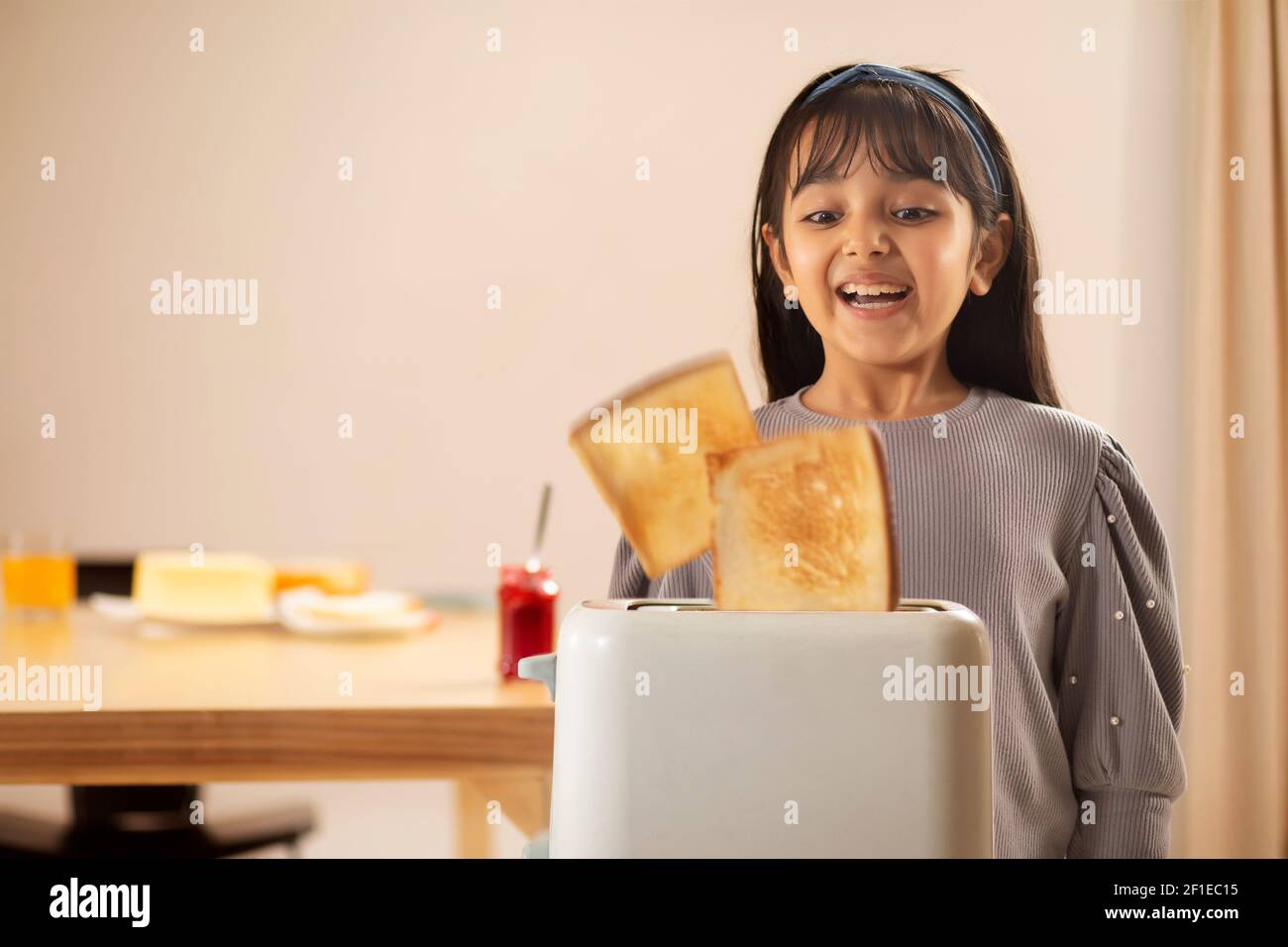 A HAPPY GIRL LOOKING AT BREAD TOAST POPPING OUT OF A TOASTER Stock Photo