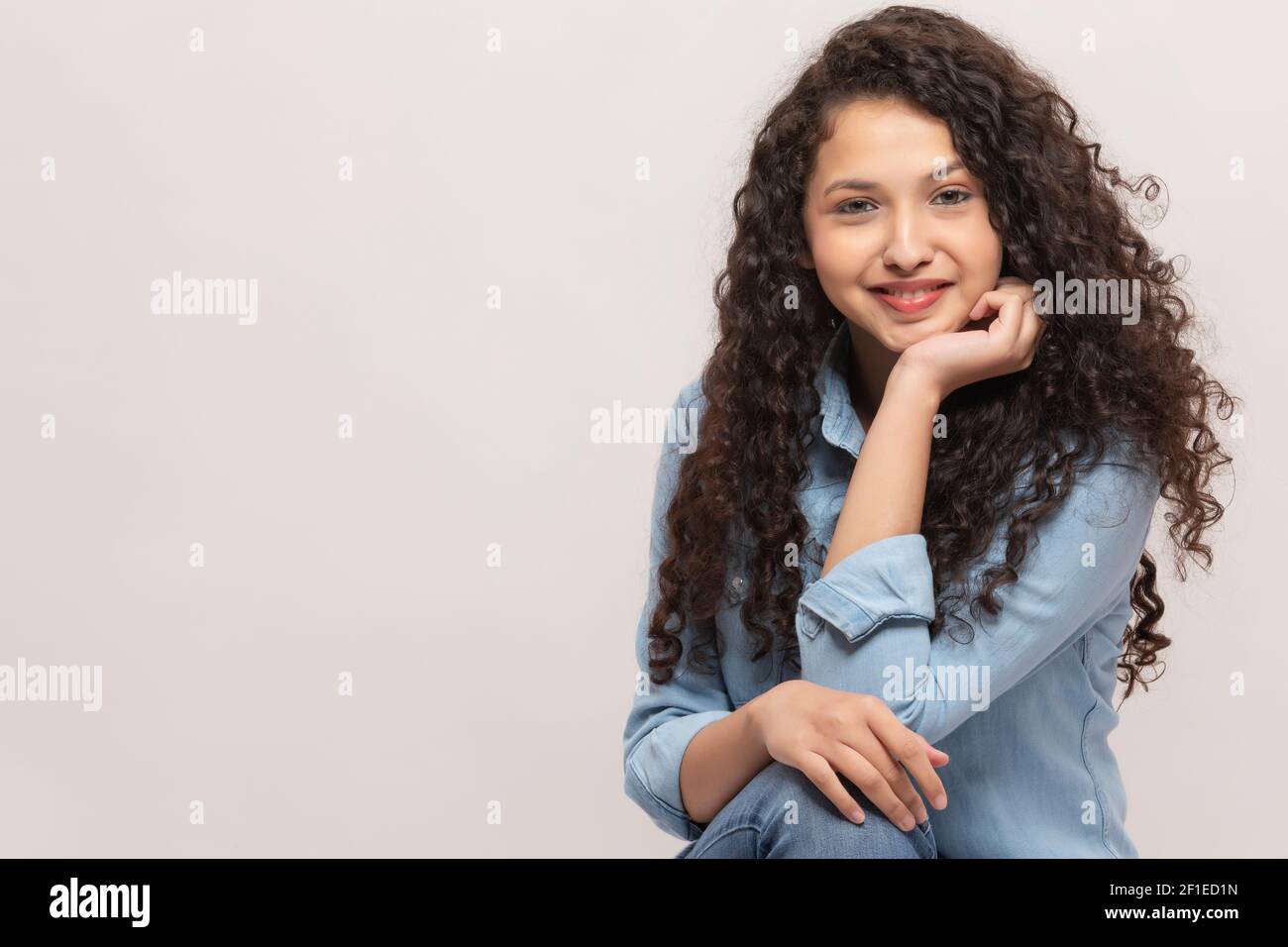 PORTRAIT OF A CURLY HAIRED TEENAGE GIRL LOOKING AT CAMERA AND SMILING ...