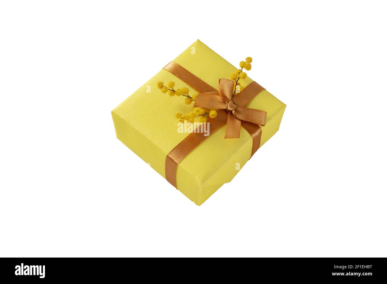 Spring holidays gift box with golden ribbon bow and mimosa flowers isolated on white. Present wrapped with yellow paper. Stock Photo