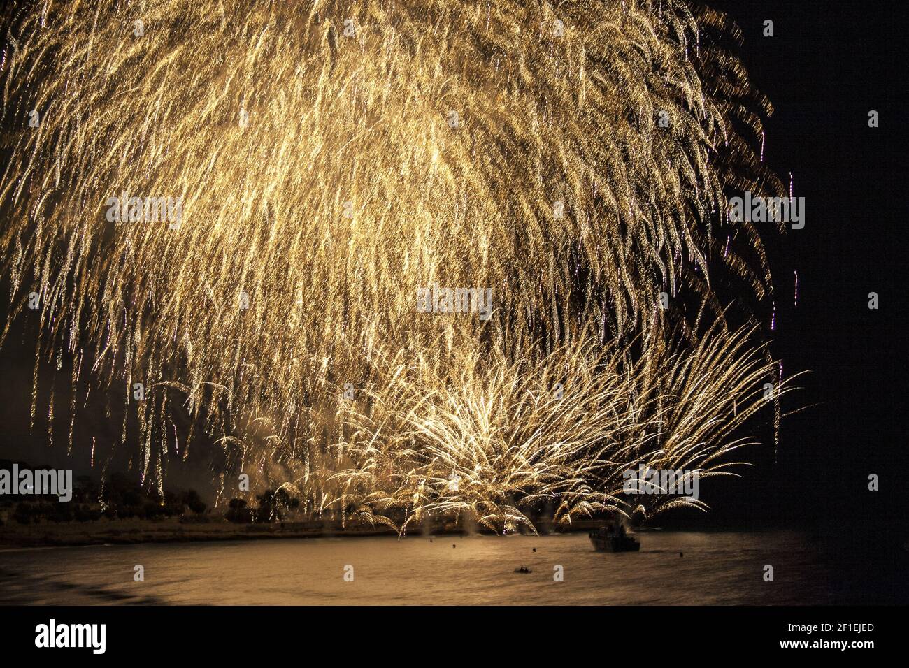 Golden fireworks falling over sea with reflections Stock Photo