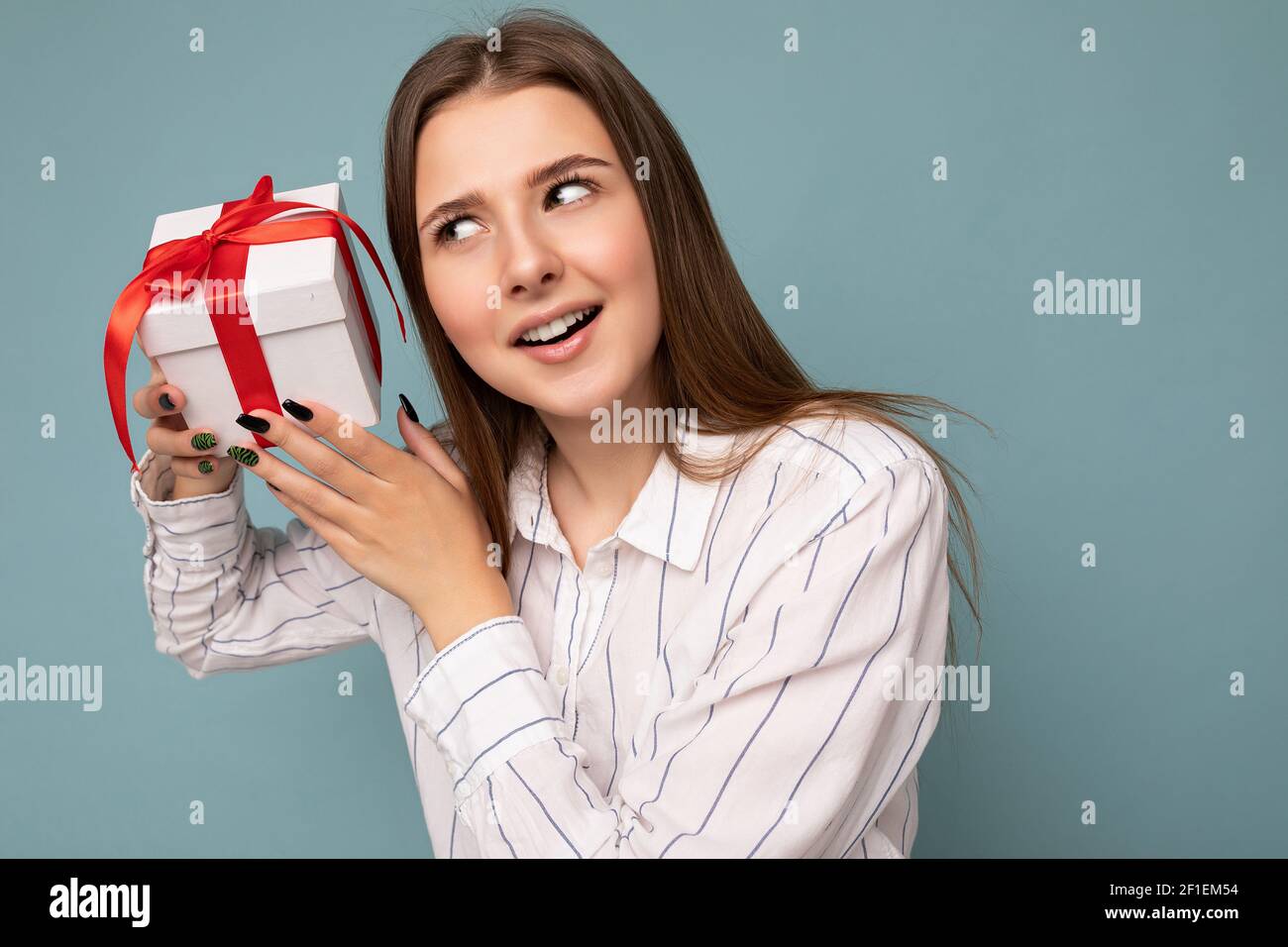 Photo shot of pretty positive surprised young dark blond woman isolated over colourful background wall wearing trendy outfit look holding gift box and Stock Photo