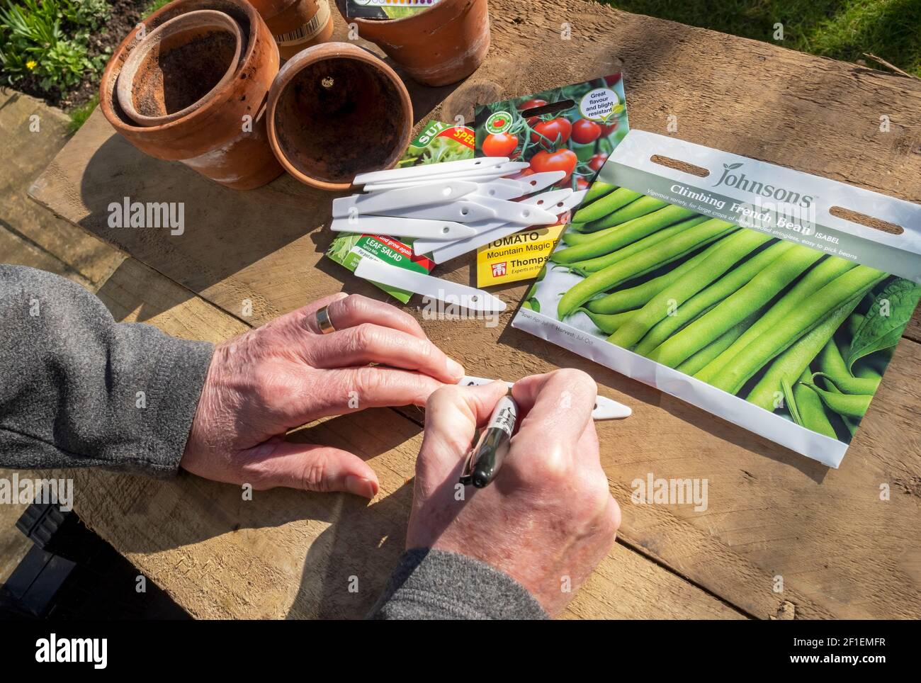 Close up of man person gardener writing plant label and packets of vegetable seed seeds on a table England UK United Kingdom GB Great Britain Stock Photo