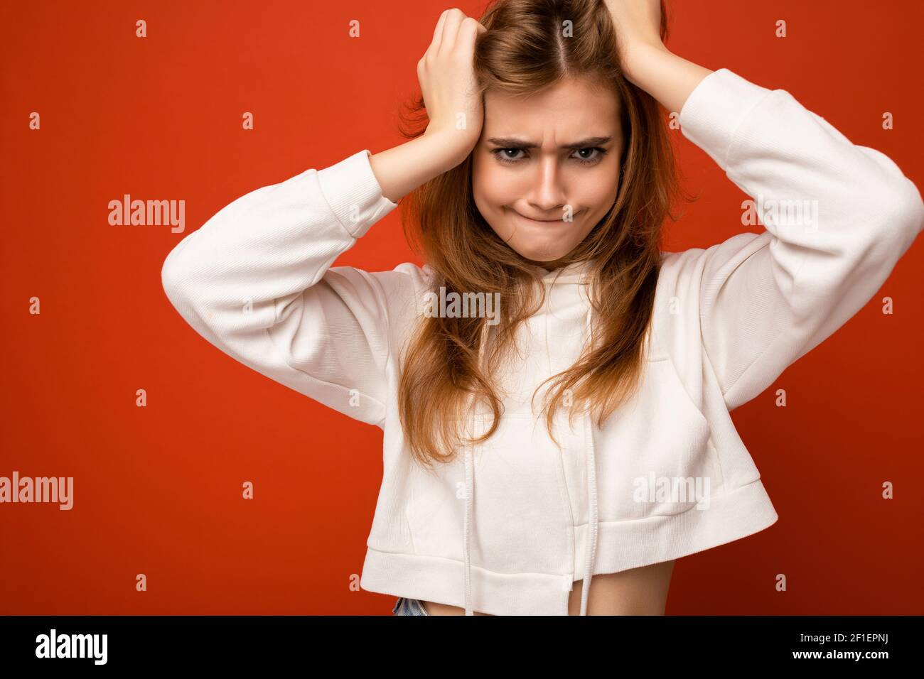 Young angry funny dark blonde woman with sincere emotions isolated on background wall with copy space wearing casual white hoodie. Positive concept Stock Photo