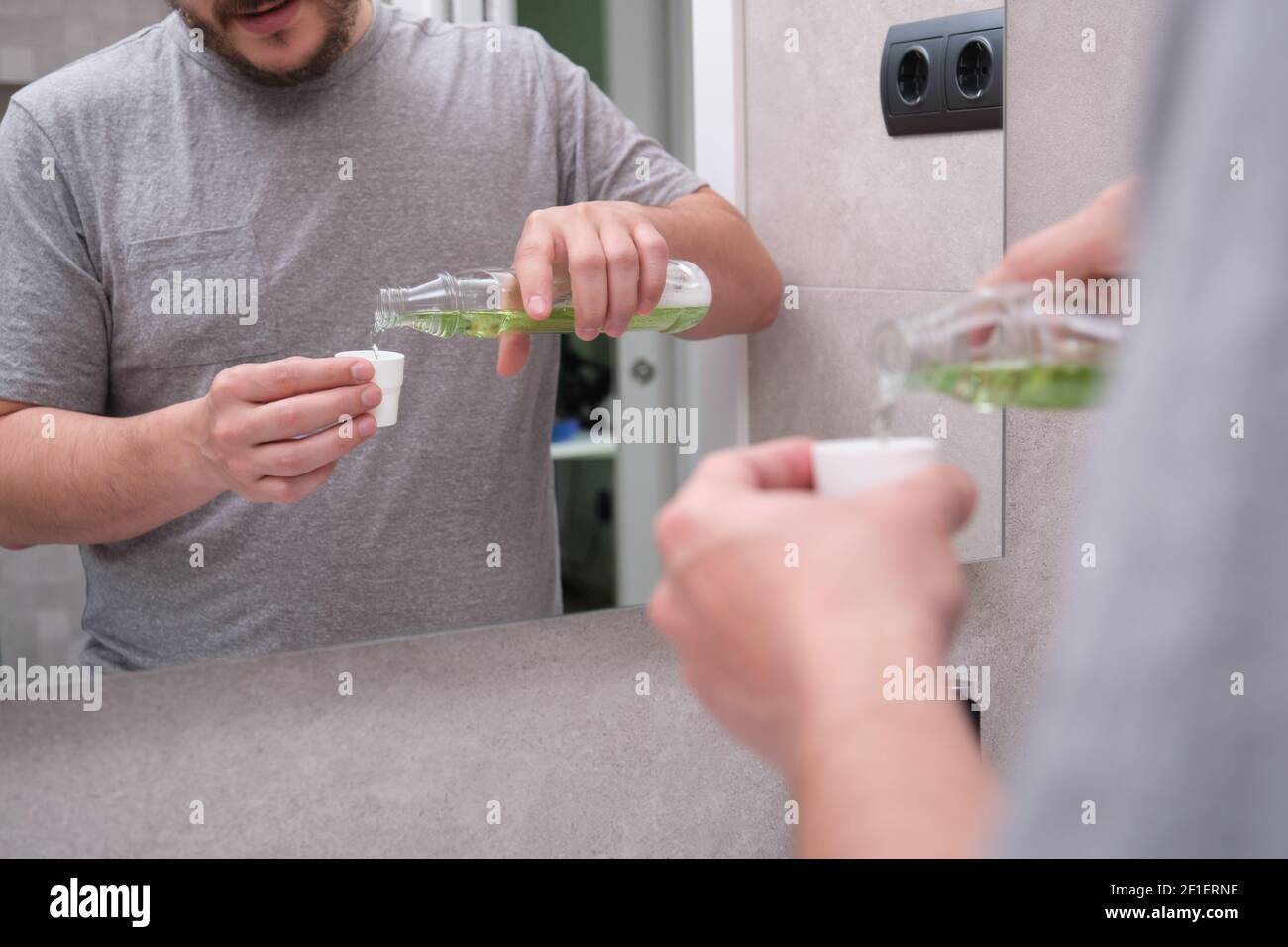 Man pouring green mouthwash from bottle into cap in bathroom. Teeth care concept Stock Photo Alamy