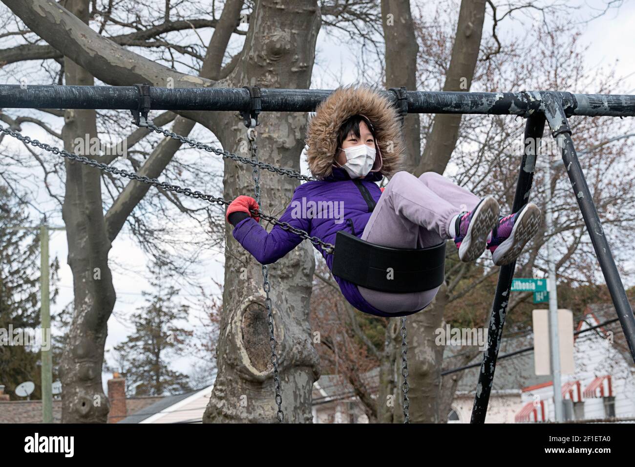 A masked happy Asian American teenager flys high on a swing in Kissena Park, Flushing, New York Stock Photo