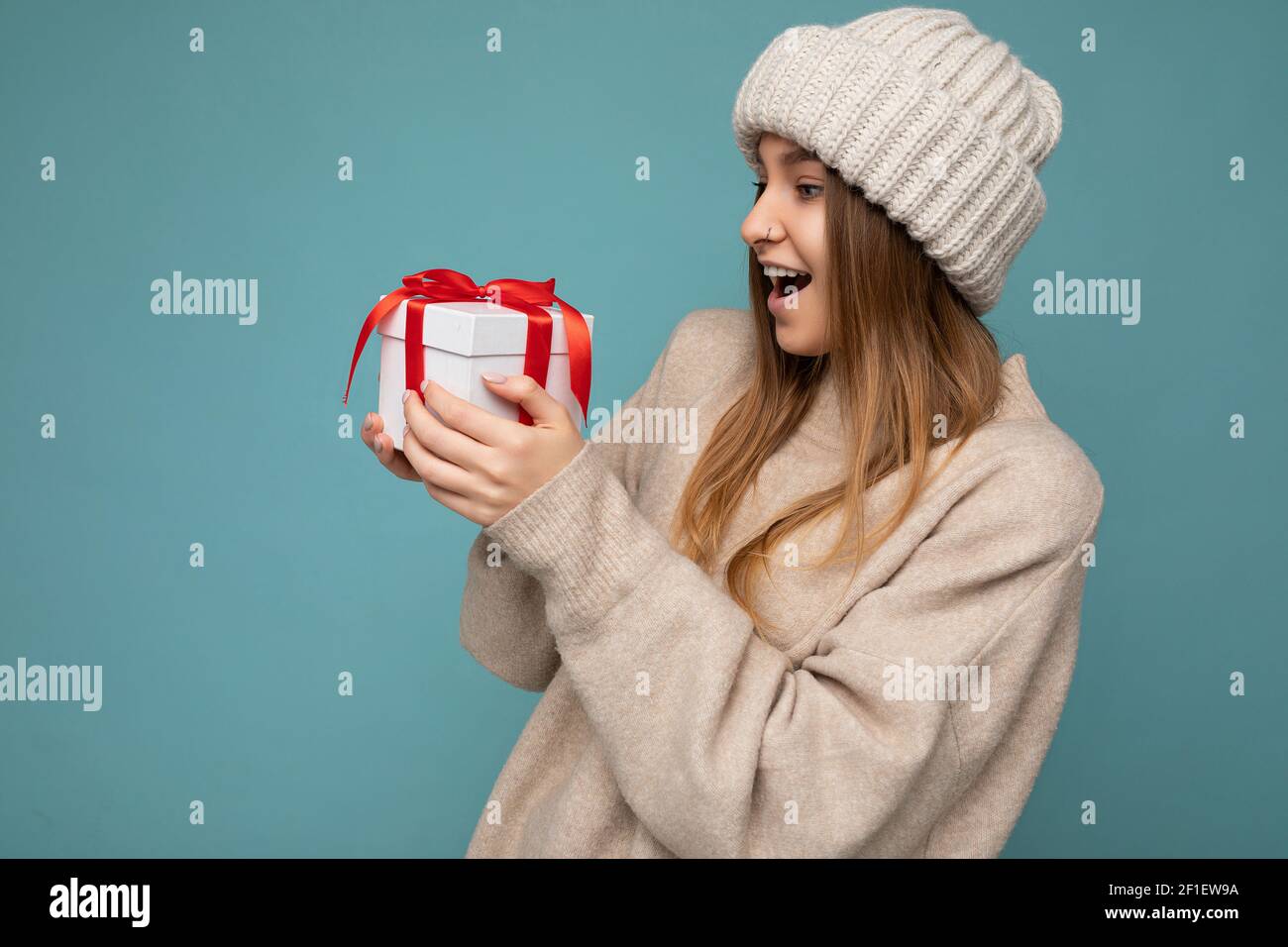 Shot of fascinating happy amazed shocked dark blonde adult woman isolated over blue background wall wearing casual sweater and trendy knitted hat Stock Photo
