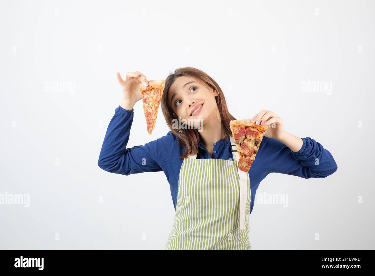 Portrait of woman in apron holding slice of pizza on white background ...