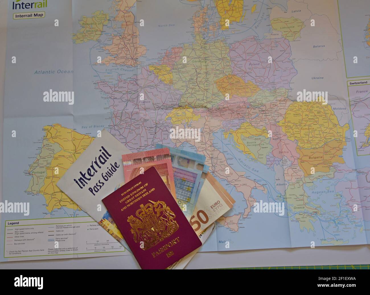 A British Passport stuffed with Euro banknotes with an Interrail guide laying on an Interrail map of Europe, ready to travel by rail across Europe Stock Photo