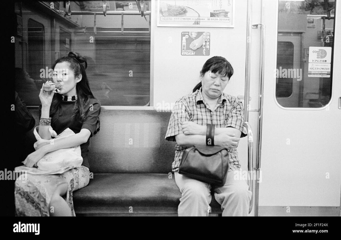 Tokyo, Japan. Sscene at the Tokyo Subway, with a sit young beautiful girl drinking, and a mature woman sleeping. Stock Photo