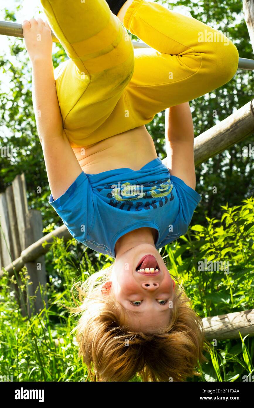 Close up portrait of cute boy hanging upside down on nature background. Smile. Tricky glance. Shaggy hair. Good mood and positive emotions. Stock Photo