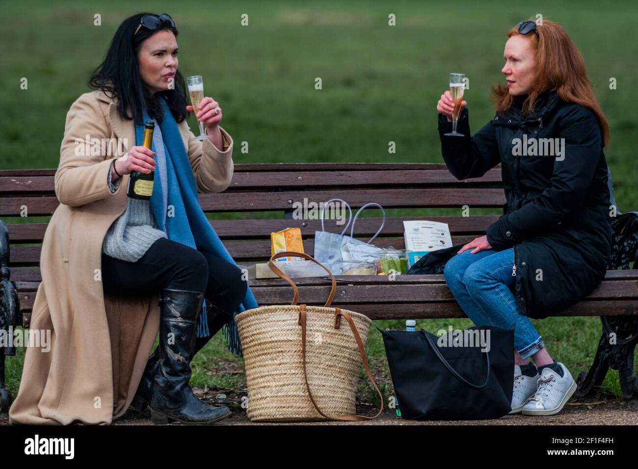 London, UK. 8th Mar, 2021. A couple of female friends meet up for a picnic with celebratory champagne as it is allowed today for the first time this year. It is dry but cold and people are out meeting friends as they take advantage of the slightly eased restrictions today. Outdoor life on Clapham Common as Lockdown 3 begins to ease a little . Credit: Guy Bell/Alamy Live News Stock Photo