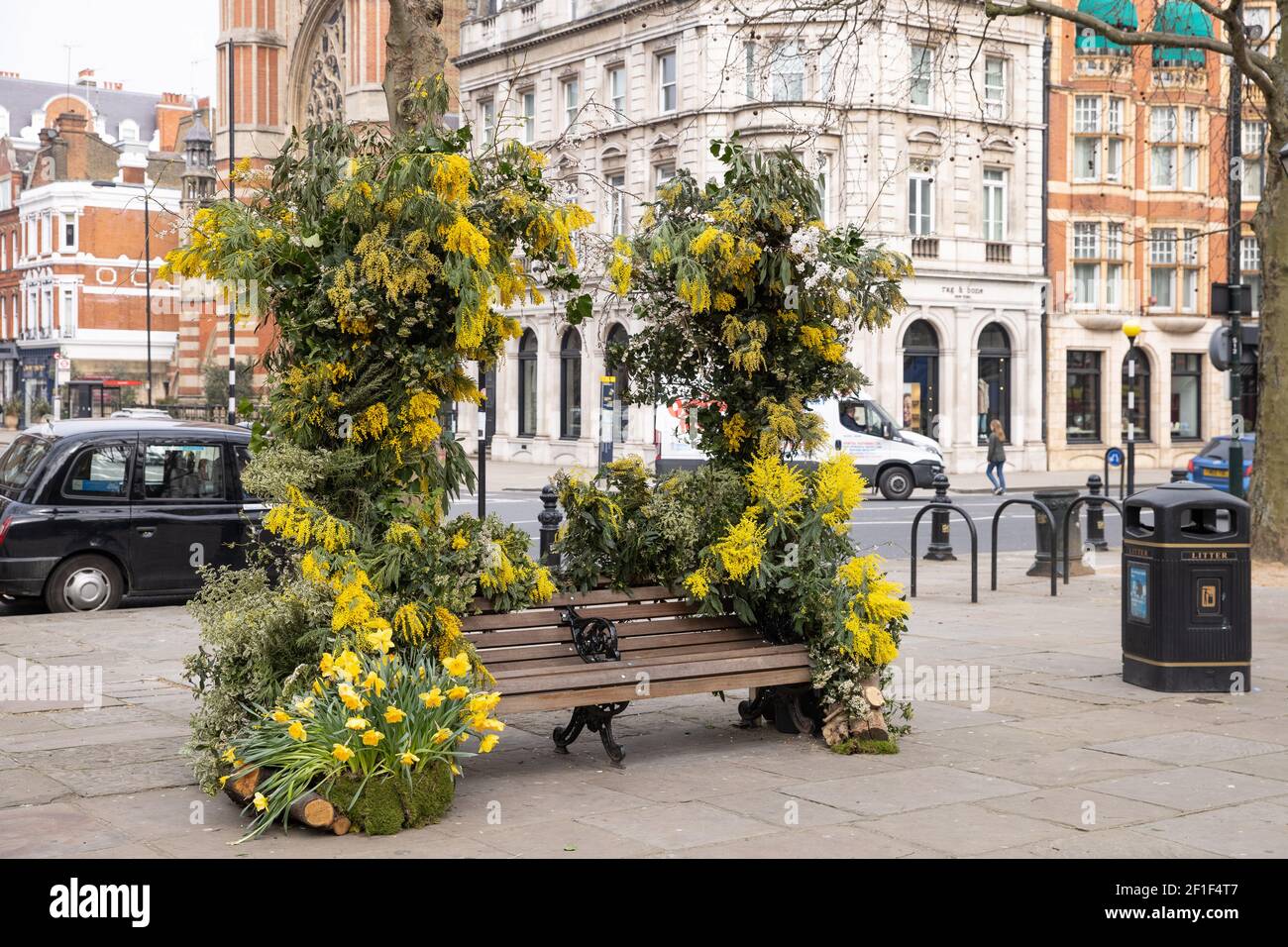 A flower decorated bench.London event florist,  Warren Bushaway, celebrates the International  Women's Day with a Banksy style flower arrangement in Sloane Square. Stock Photo