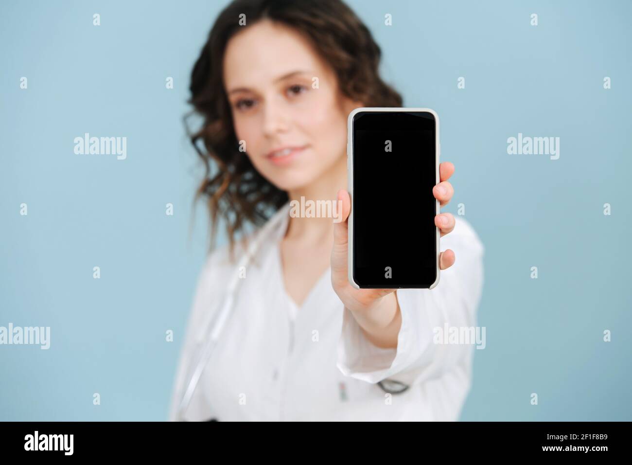 Cute beautiful female nurse holding her phone close to camera. Over ...