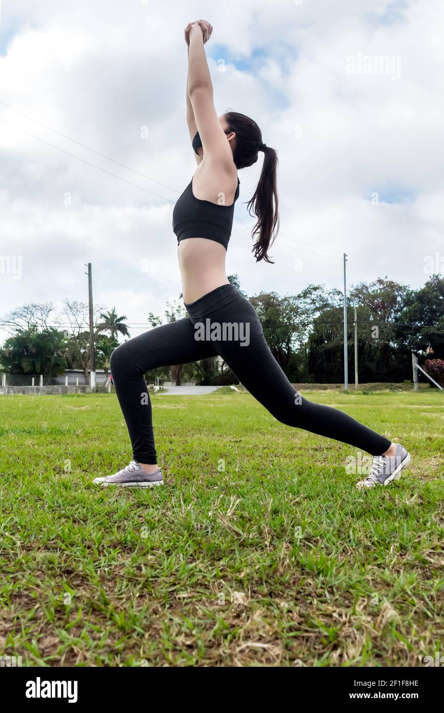 Young woman stretching outdoors on the grass while warming up before starting to work out, arms lifted towards the sky Stock Photo