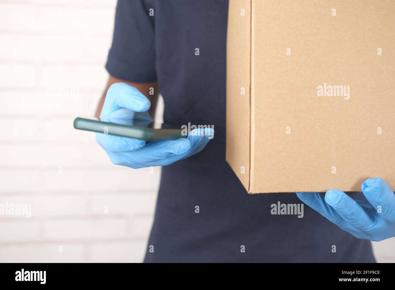 https://c8.alamy.com/comp/2F1F9CE/delivery-man-hand-in-latex-gloves-holding-smart-phone-and-card-box-2F1F9CE.jpg