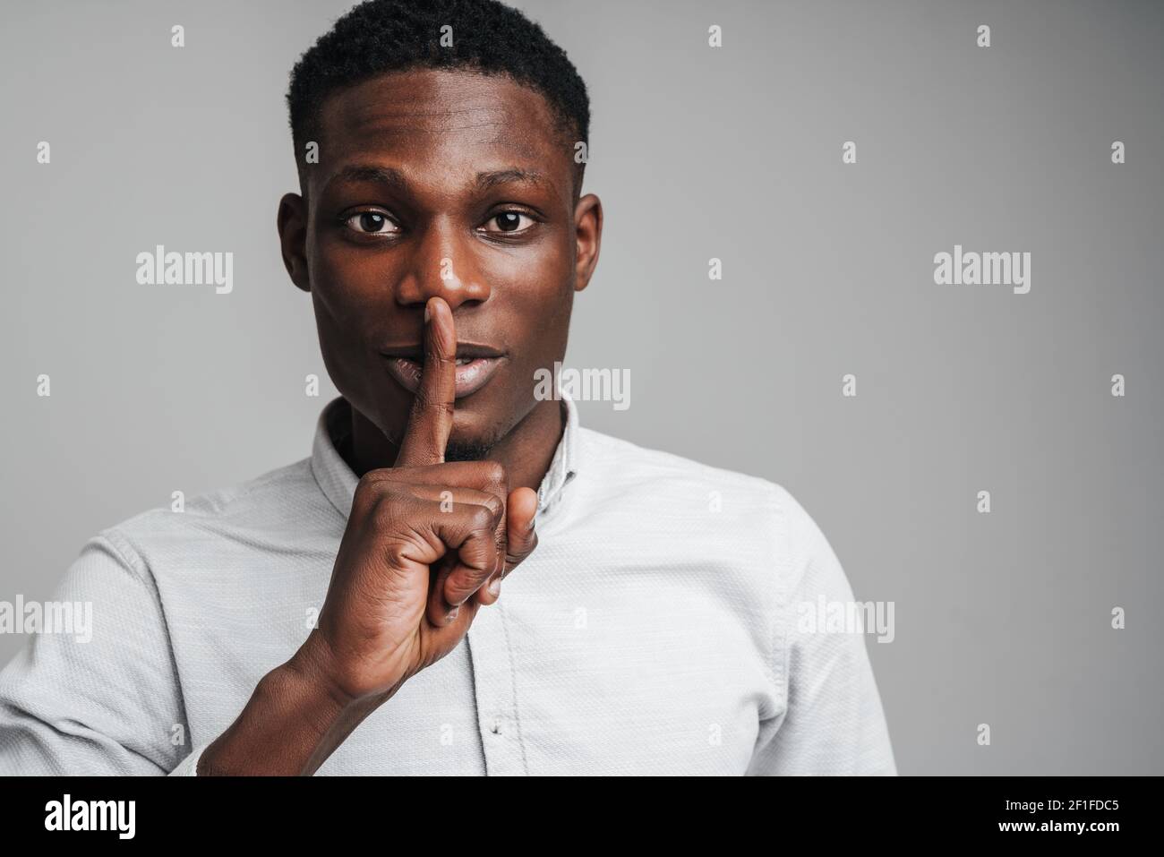 Closeup portrait young businessman placing finger on lips saying, shhh, be quiet, silence, isolated over grey background Stock Photo