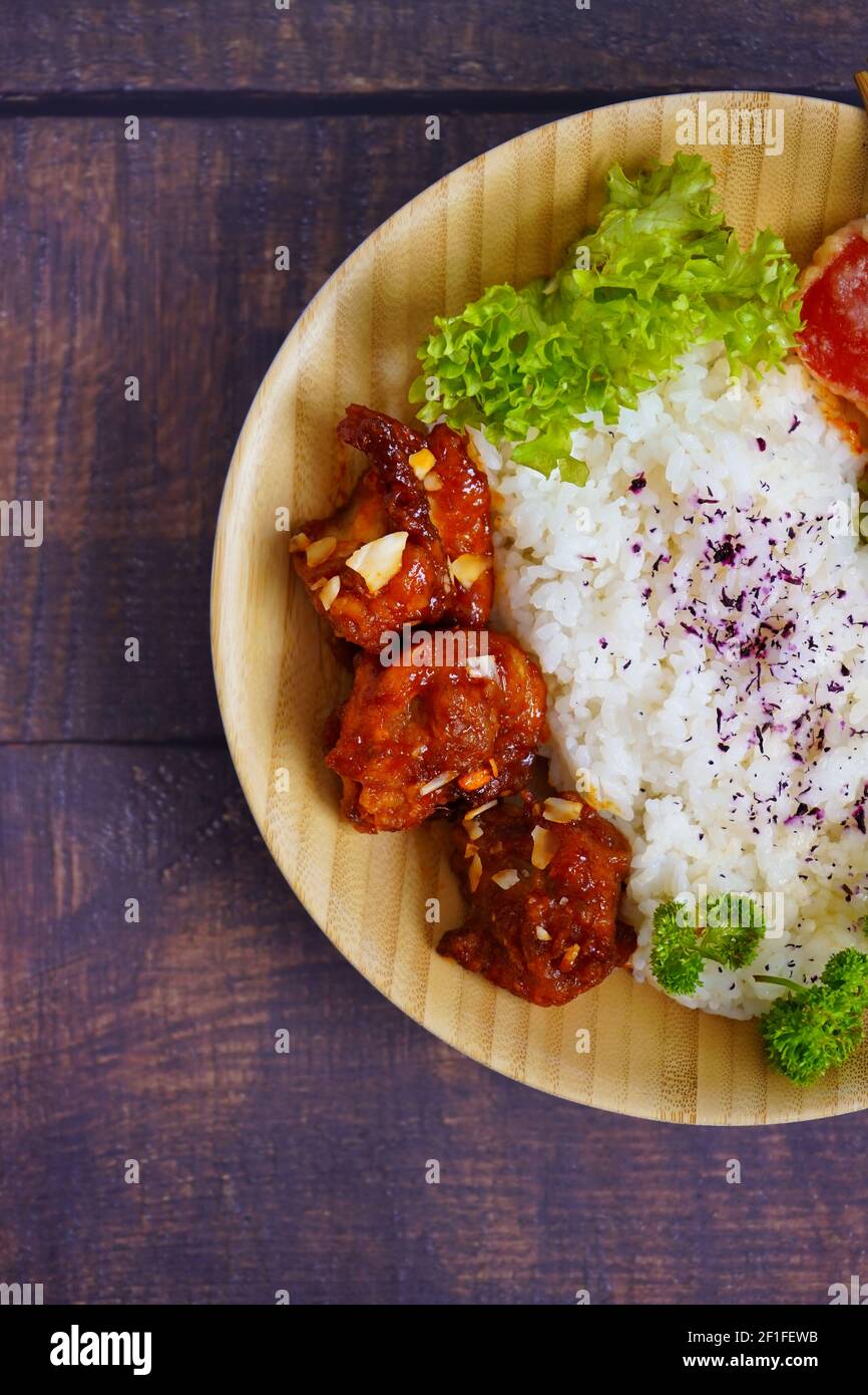 Home cooked Japanese grilled chicken dish with vegetables and rice, served on a bamboo plate. Rustic wooden table background. Stock Photo