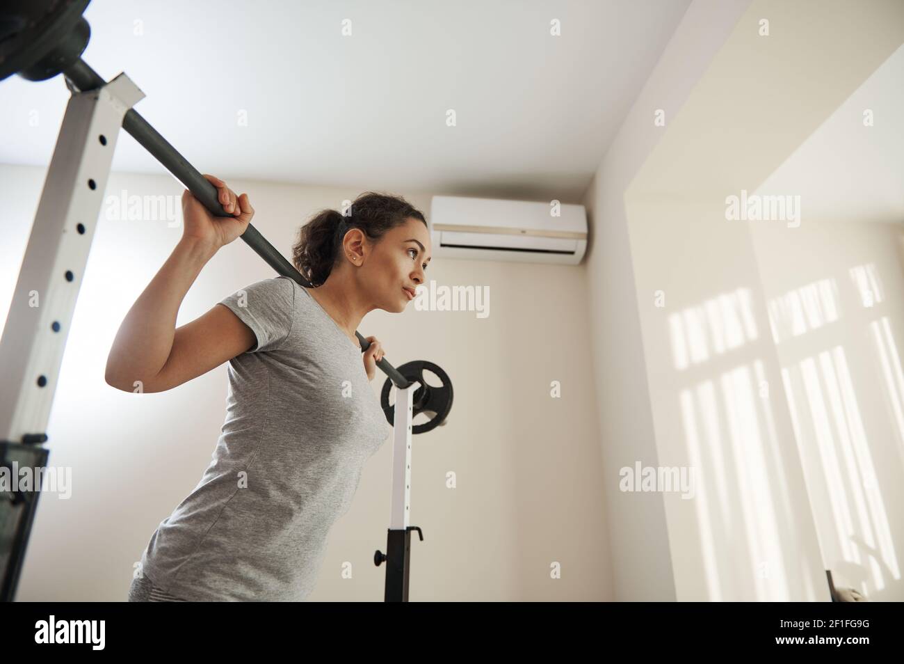 Beautiful woman training with a barbell at home. Active and healthy lifestyle concept Stock Photo