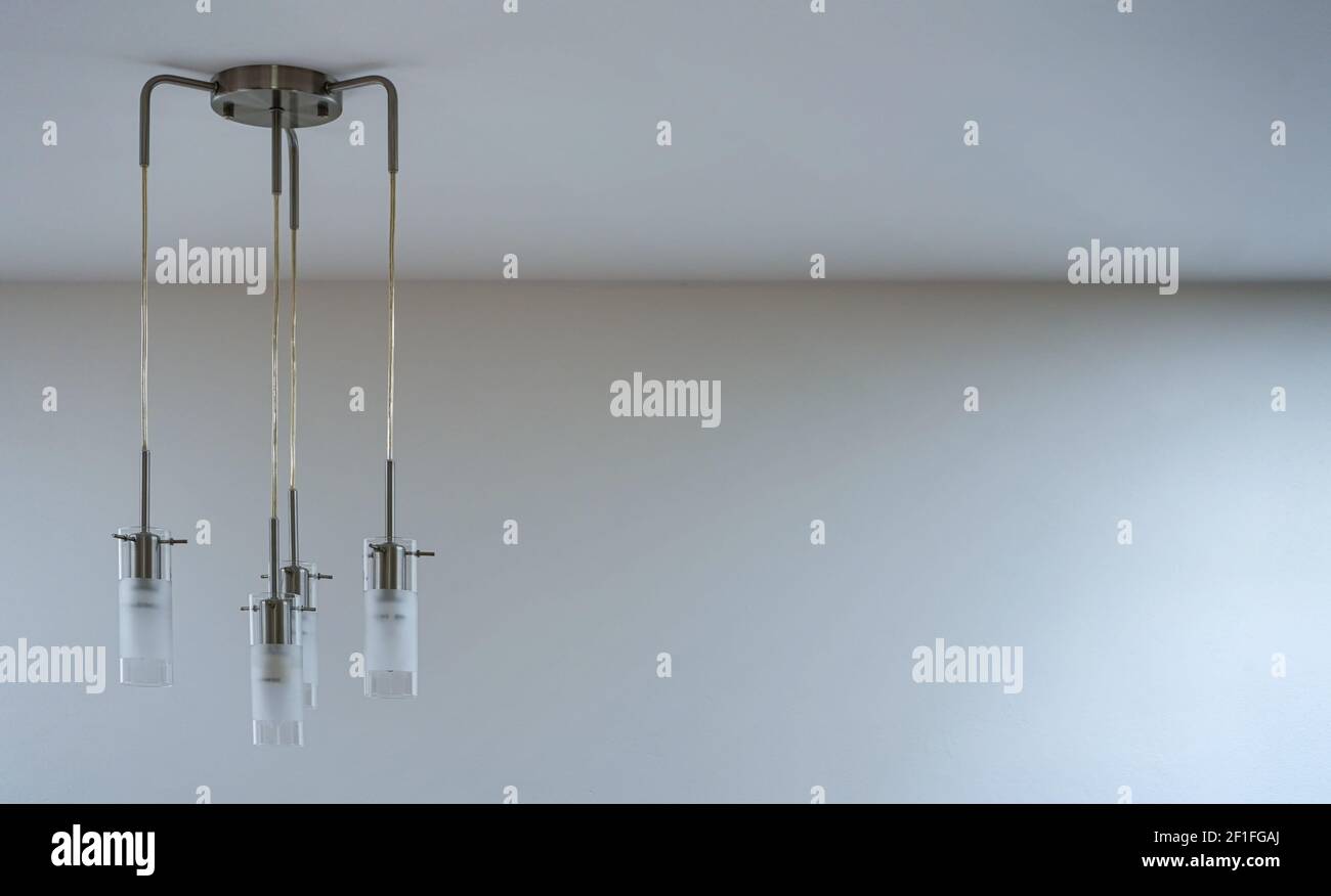 Modern metal and glass lamp with four lights hanging form the ceiling, empty space right side Stock Photo