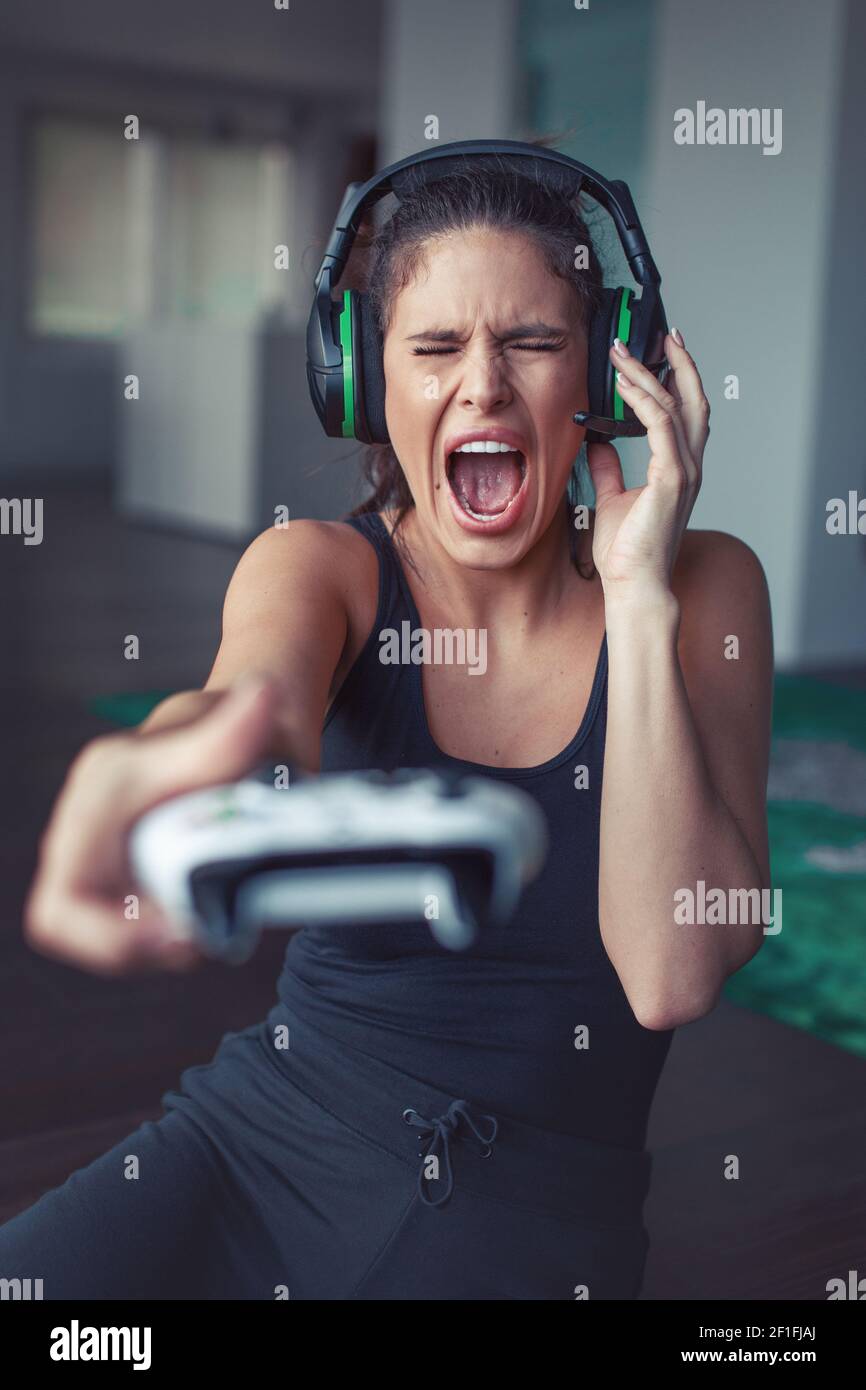 Young Caucasian gamer woman shouting into microphone while playing online, depth of field Stock Photo