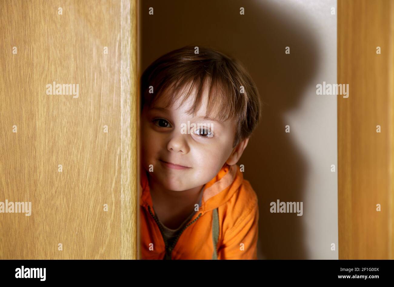 Little boy playing hide and seek in a closet. Stock Photo