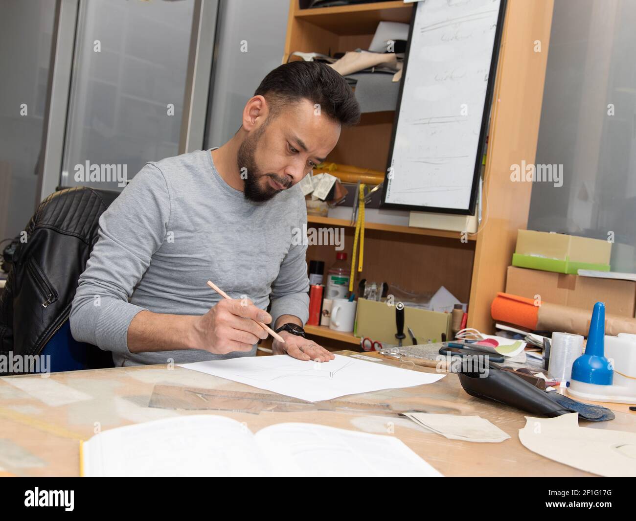 Young male immigrant working as an architect engineer designer. Doing planning work on a busy desk in the office. Stock Photo