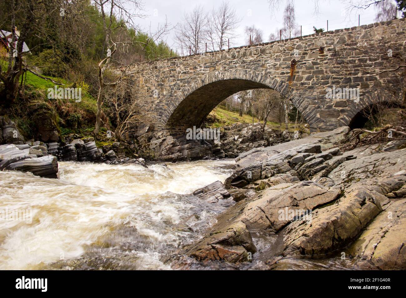 A single arched stone bridge crossing the fast flowing Feshie River in ...