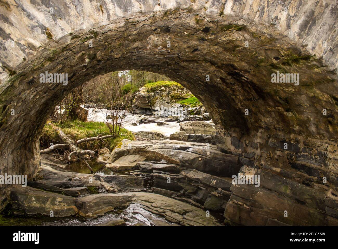 A single arched stone bridge crossing the fast flowing Feshie River in ...
