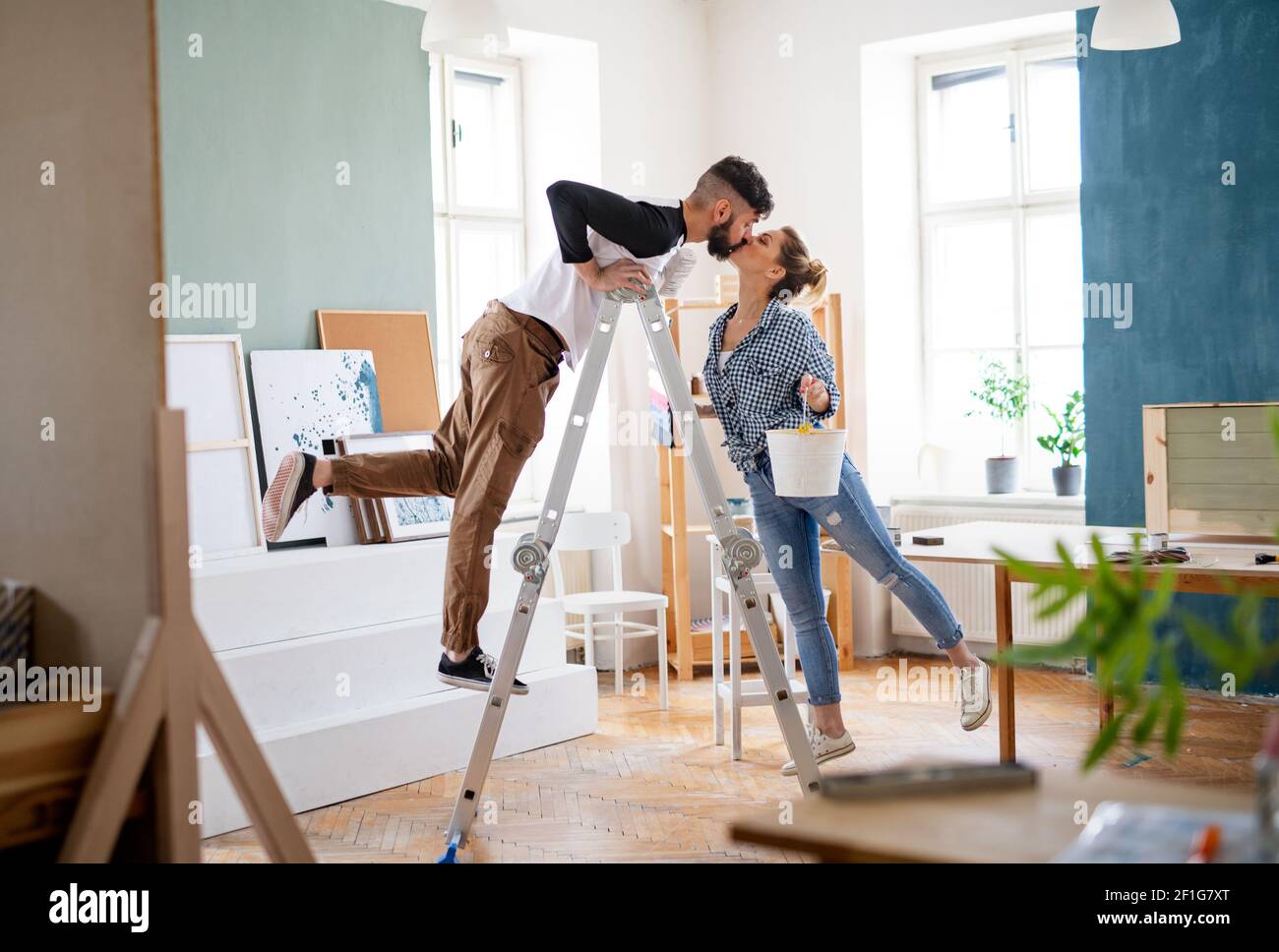 Mid adults couple kissing when painting indoors at home, relocation and diy concept. Stock Photo