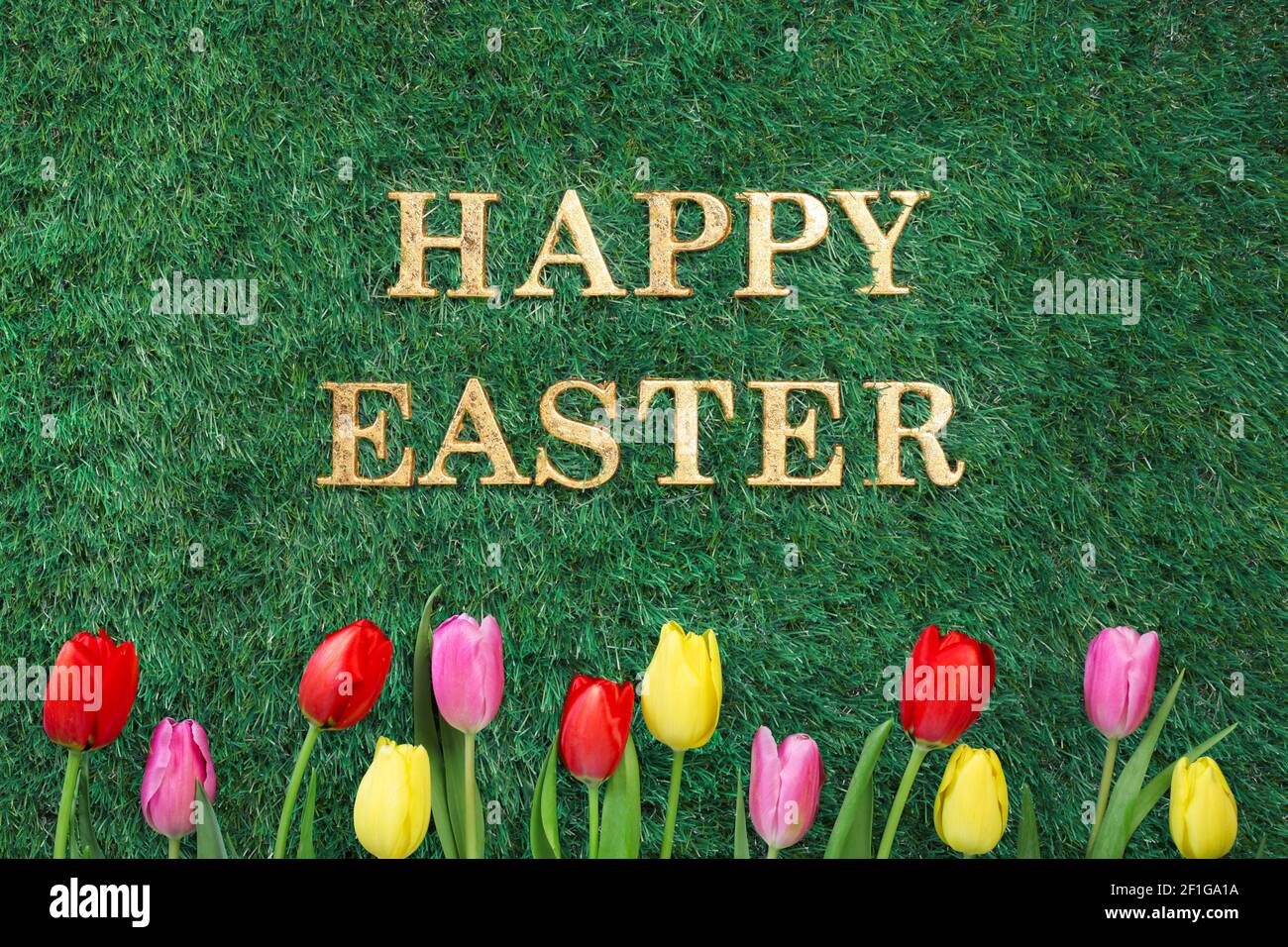 Happy Easter text on green grass with colorful tulips. Stock Photo