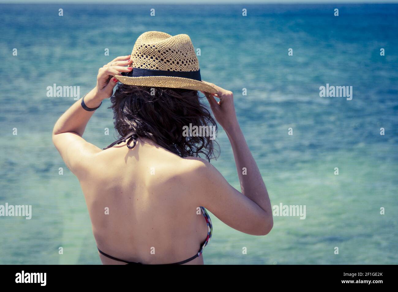 Beautiful woman in sunhat and bikini looking at the beach on a hot summer day. Photo from Fuerteventura Island, Spain Stock Photo